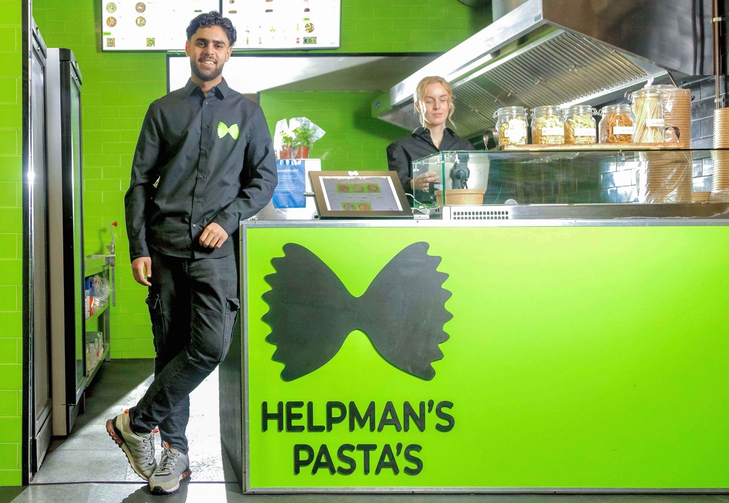 Twee teamleden bij de groene toonbank met farfalle-logo in een Helpman's Pasta's vestiging